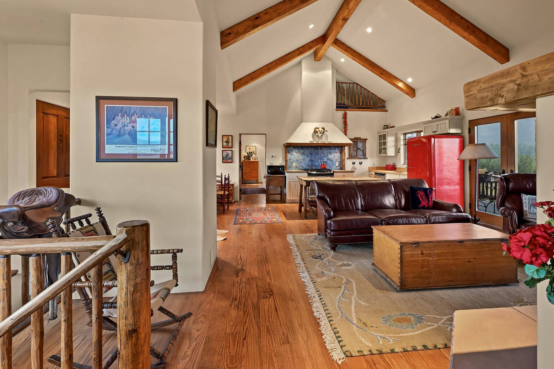 Open-concept living area with exposed wooden beams, red refrigerator, and leather sofas under a vaulted ceiling.