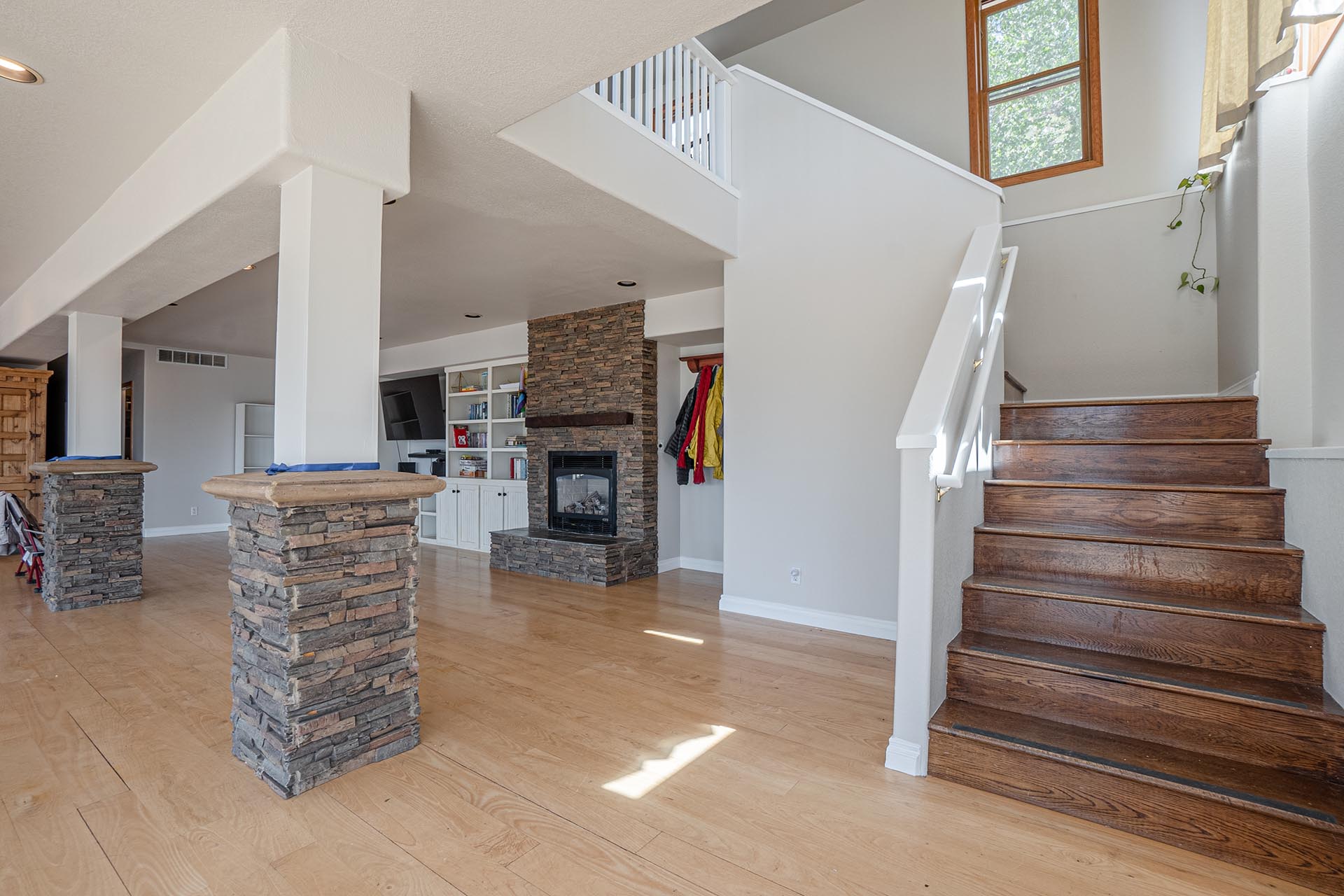 Open-concept living area with a stone fireplace, white built-ins, and an upper mezzanine overlooking the space.