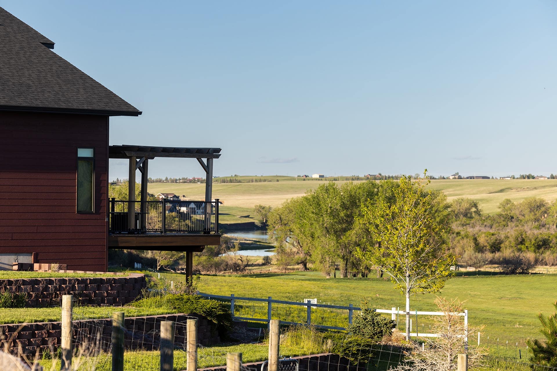Red wooden house with a second-story balcony overlooking a green rural landscape and distant hills.