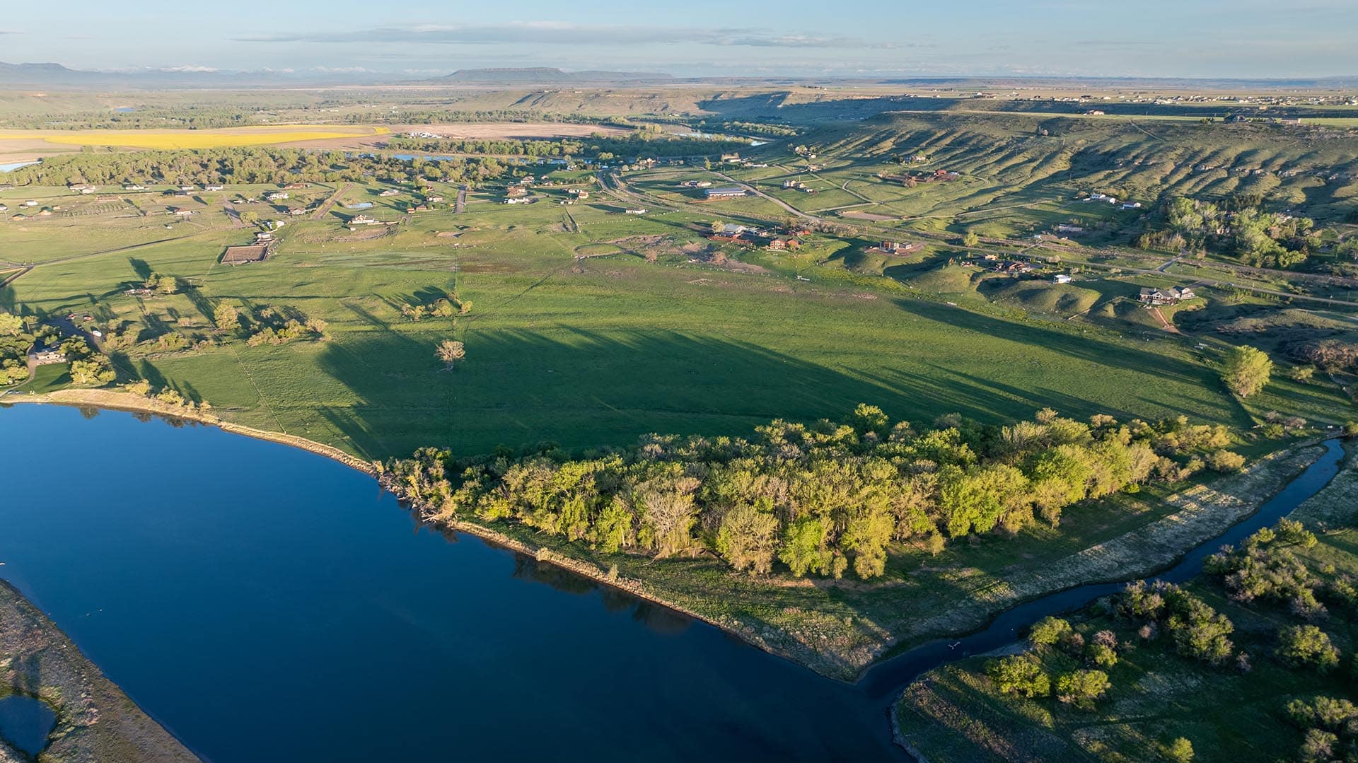 Aerial view of a river winding through green fields and small houses in a rural valley.