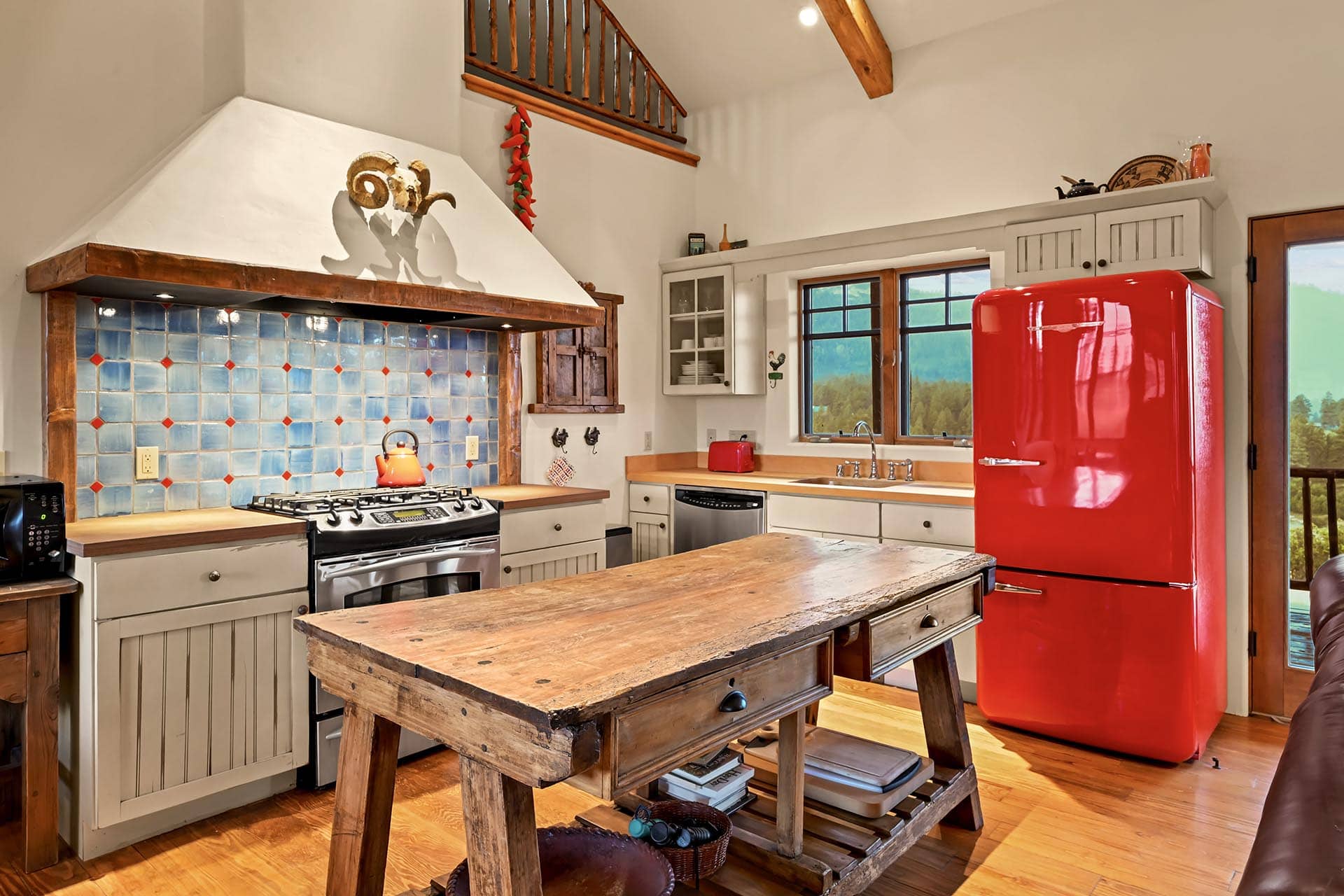 Rustic kitchen with a bright red refrigerator, blue tiled backsplash, and a wooden island center stage.