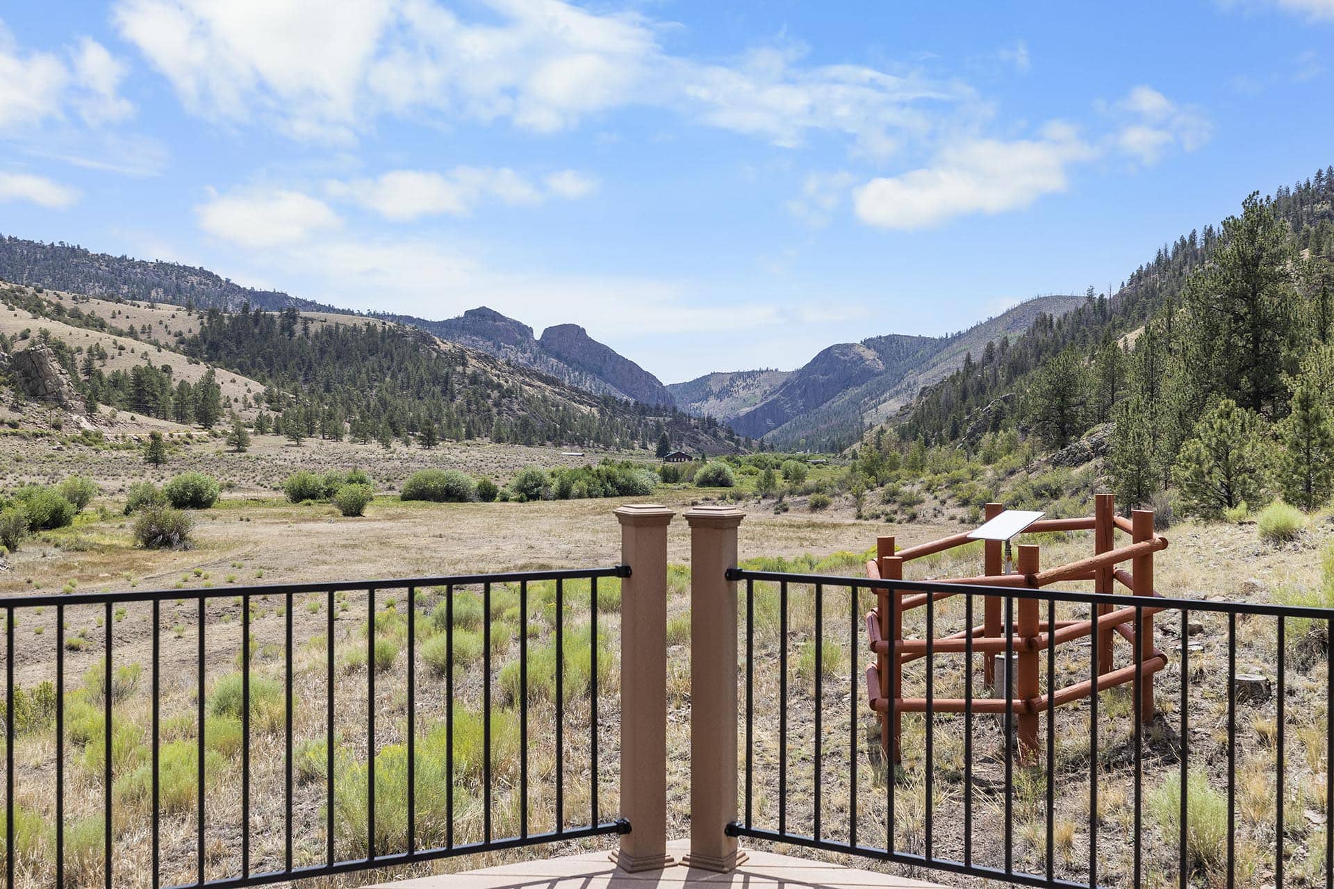 View of a desert valley and mountains through a black metal railing on a deck.