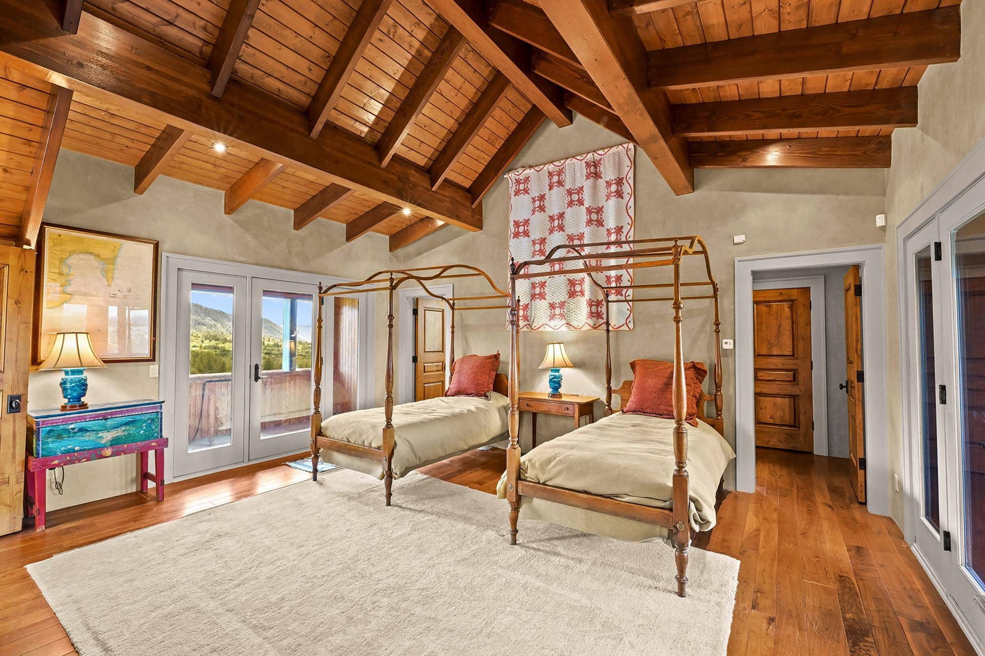 Bedroom with exposed wooden beams, two antique four-poster beds, and a quilted wall hanging above the beds.