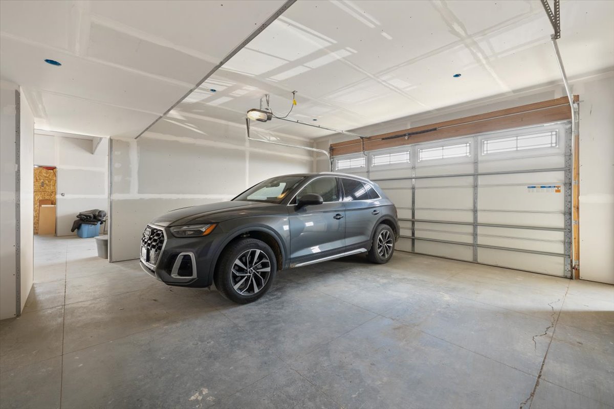 New gray SUV parked inside a spacious, unfinished garage with a large door.